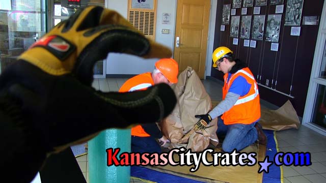Kansas CIty Crates safety compliance officer makes funny photo with cut resistance glove by posing index finger and thumb over hard hat of project manager