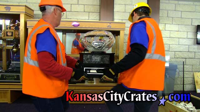 Crate personnel wearing orange safety vests carry trophy to display case for temporary storage during reconstruction of Vanier Family Football Complex that will be used by all 16 K-State Varsity Sports