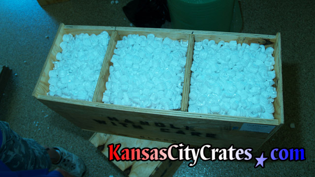 View before closing crate filled with packing peanuts containing three delicate light fixtures.