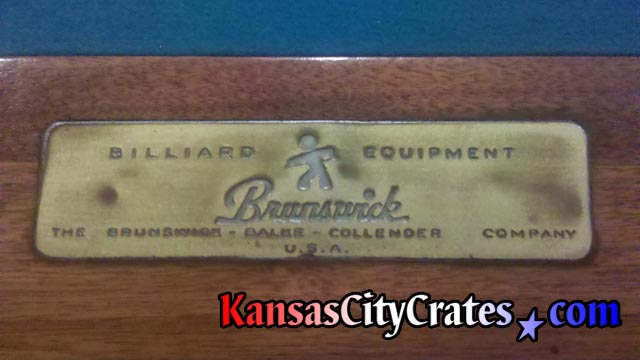 Antique name plate of the Brunswick-Balke-Collender Company at head of billiard table on rail.