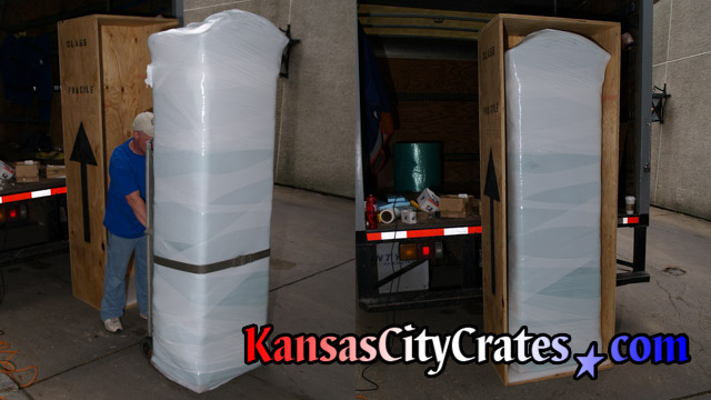 Large grandfather clock case that is paper, bubble and stretch wrapped loading into solid wall export crate for shipping at company truck.