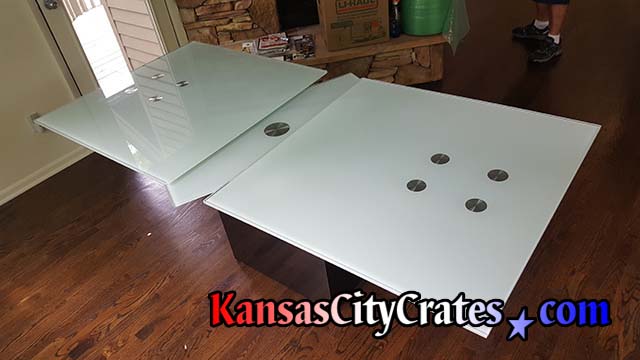 Outside leafs of expandable glass dining table are removed for crating while center rotating glass remains on mechanical frame base
