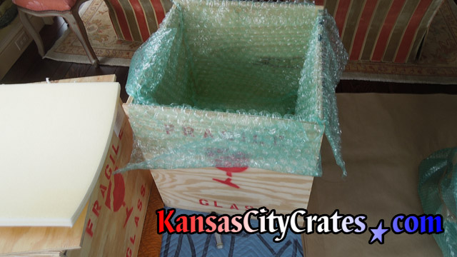 Foam cushioning is placed on bottom of wood crate before bubble wrap is layed inside.
