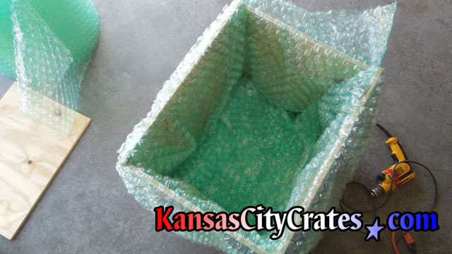 Top view of wood crate with foam cushioning on shipping edge and a blanket of bubble wrap before placing fragile inside for shipping at home in Weston MO  64098