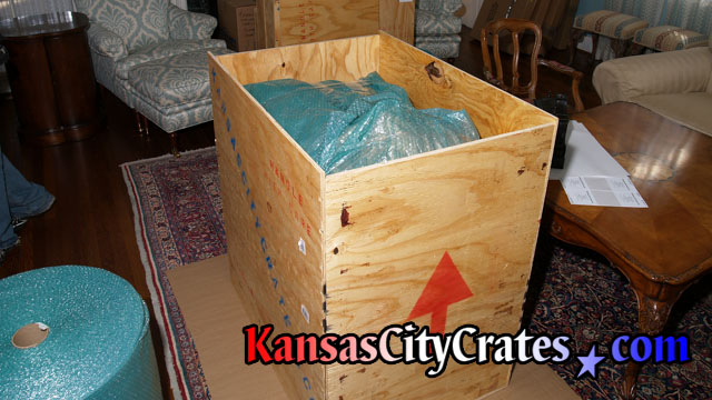 Vase surrounded by foam and bubble wrap inside vault like wood crate.